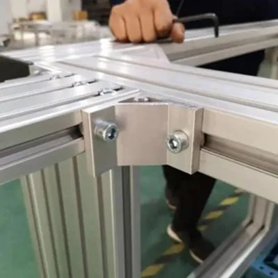 Close-up of silver T-slot aluminum extrusion profiles connected with heavy-duty corner bracket and bolts during assembly of modular machine frame system By Yoverd Aluminium