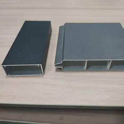 Close-up of two premium aluminum privacy screen railing profiles—one matte black rectangular hollow section and one gray multi-chamber textured panel—displayed on a light wood tabletop for modern residential and commercial applications by Yoverd Aluminium.